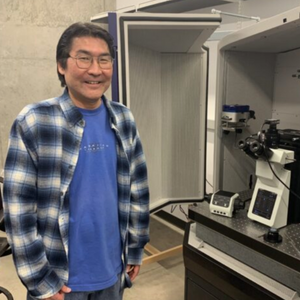 photo of Gregory Uyeda standing next to microscope