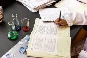 a student takes notes in her lab notebook in a lab surrounded by beakers and data